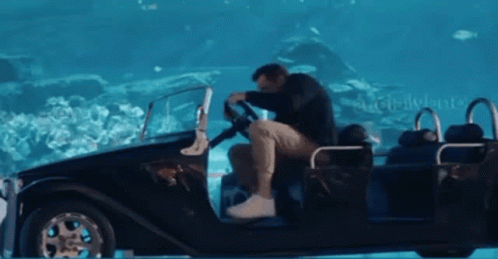 A Man Is Sitting In A Car That Is Floating In The Water With The Word Disneyland In The Background GIF