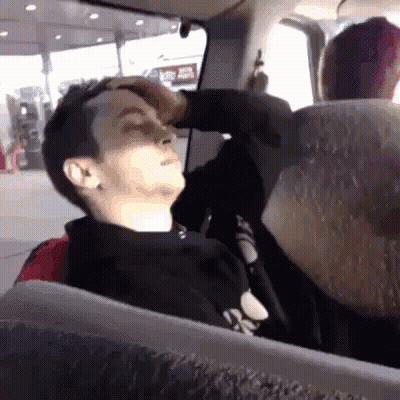 A Man Is Sitting In A Car With His Eyes Closed And His Hand On His Forehead GIF