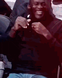 A Man Is Sitting In A Chair And Smiling While Holding A Piece Of Food . GIF