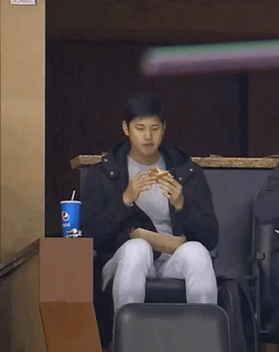 A Man Is Sitting In A Chair Eating A Hamburger And Drinking Pepsi . GIF