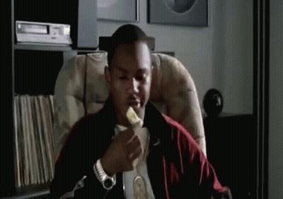 A Man Is Sitting In A Chair Eating A Piece Of Banana . GIF