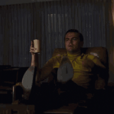 A Man Is Sitting In A Chair Holding A Cup Of Coffee And Pointing At Something With The Words Look A Slacker Written Belo GIF
