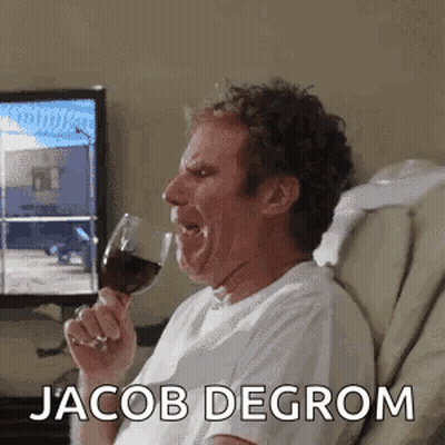 A Man Is Sitting In A Chair Holding A Glass Of Wine And Making A Funny Face . GIF