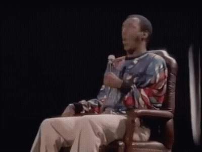 A Man Is Sitting In A Chair Holding A Microphone And Talking Into It . GIF