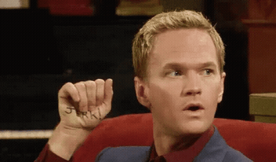 A Man Is Sitting In A Chair Holding A Piece Of Paper With The Word Jerk Written On His Hand . GIF