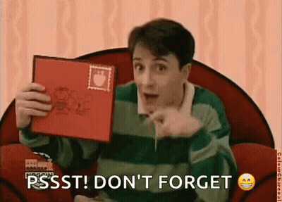 A Man Is Sitting In A Chair Holding A Red Book And Pointing At The Camera . GIF