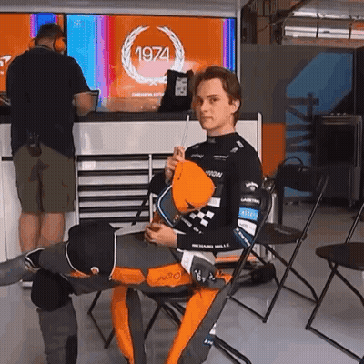 A Man Is Sitting In A Chair In Front Of A 1974 Sign GIF