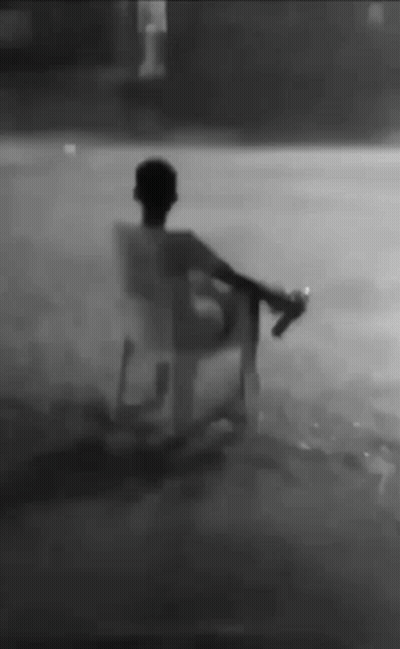 A Man Is Sitting In A Chair In The Rain Holding A Bottle . GIF