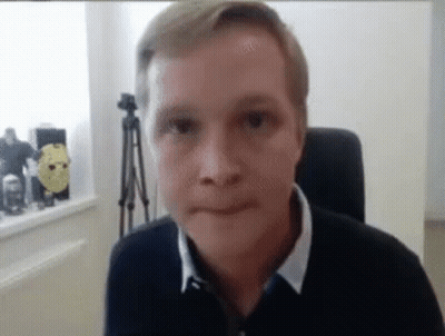 A Man Is Sitting In A Chair Looking At The Camera And Making A Face . GIF