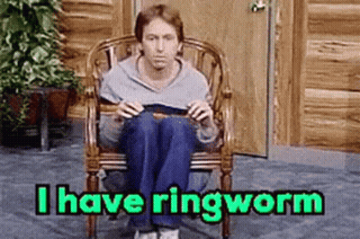 A Man Is Sitting In A Chair Reading A Book With The Words I Have Ringworm Above Him . GIF