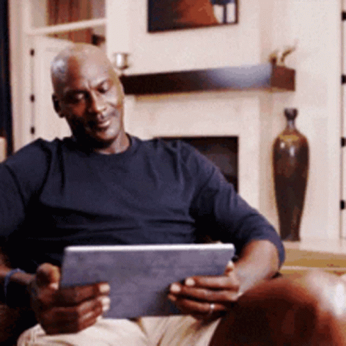 A Man Is Sitting In A Chair Using A Tablet Computer GIF