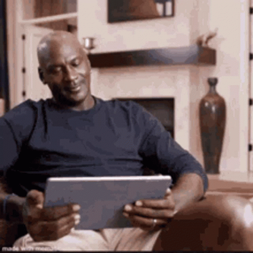 A Man Is Sitting In A Chair Using A Tablet Computer . GIF