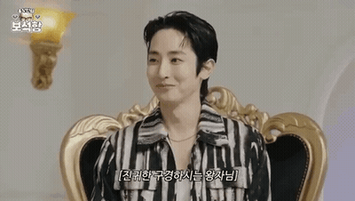 A Man Is Sitting In A Chair Wearing A Striped Shirt And A Necklace . GIF