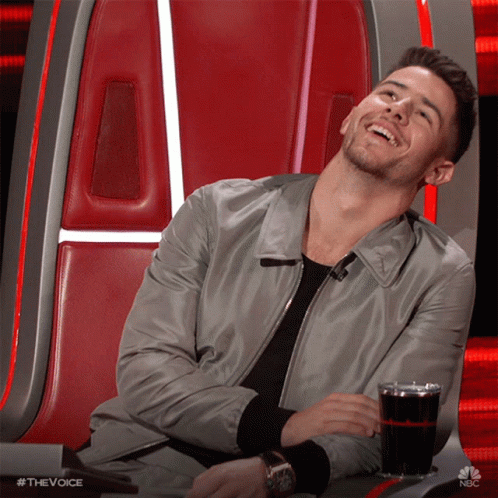 A Man Is Sitting In A Chair With A Glass Of Soda In Front Of Him And The Words #Thevoice Are On The Bottom GIF