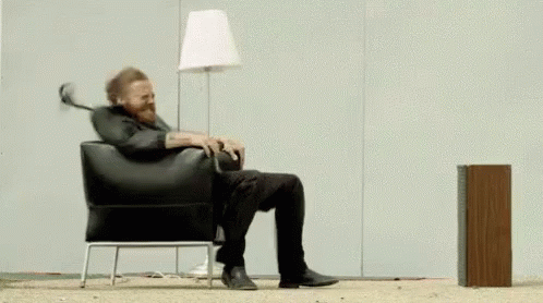 A Man Is Sitting In A Chair With A Lamp On His Head . GIF