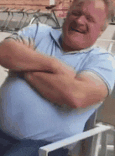A Man Is Sitting In A Chair With His Arms Crossed And Making A Funny Face . GIF