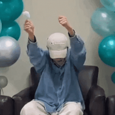 A Man Is Sitting In A Chair With His Arms In The Air And Holding A Balloon . GIF