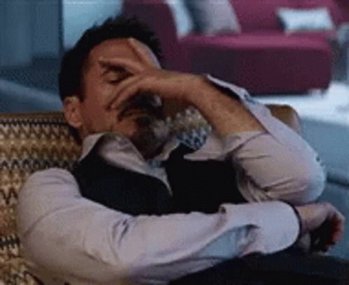 A Man Is Sitting In A Chair With His Hand On His Face . GIF