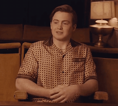 A Man Is Sitting In A Chair With His Hands Folded In Front Of A Lamp GIF