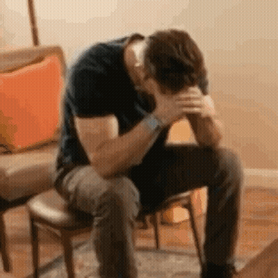 A Man Is Sitting In A Chair With His Hands On His Head . GIF