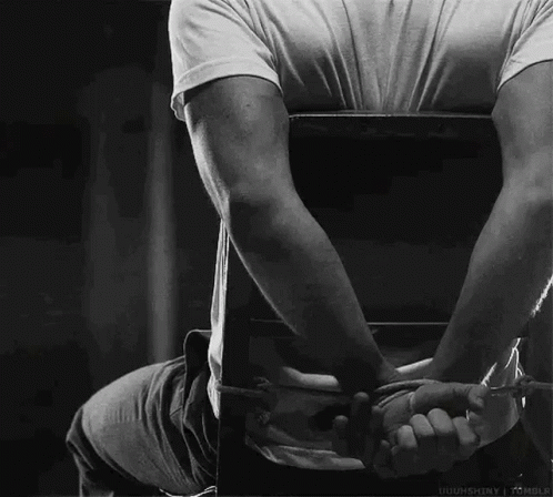 A Man Is Sitting In A Chair With His Hands Tied Behind His Back In A Black And White Photo . GIF