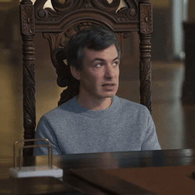 A Man Is Sitting In A Chair With Uhh Sure Written On The Table GIF