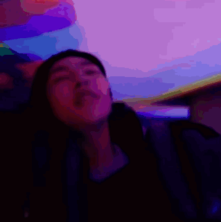 A Man Is Sitting In A Dark Room With A Purple Background And A Foreign Language Written On The Bottom GIF