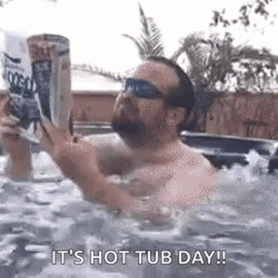 A Man Is Sitting In A Hot Tub Reading A Book While Holding A Can Of Beer . GIF