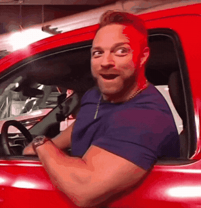 A Man Is Sitting In A Red Car With His Mouth Open GIF