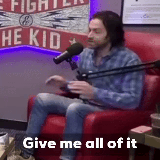 A Man Is Sitting In A Red Chair In Front Of A Microphone With The Words Give Me All Of It Below Him . GIF