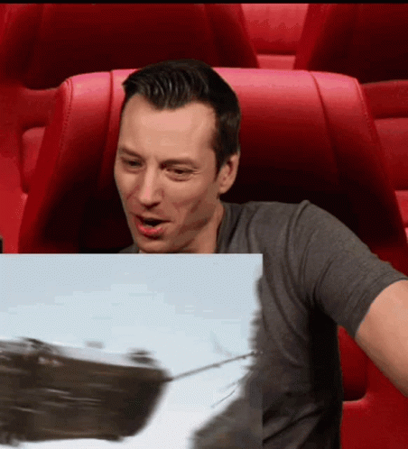 A Man Is Sitting In A Red Chair Looking At A Picture Of A Boat GIF