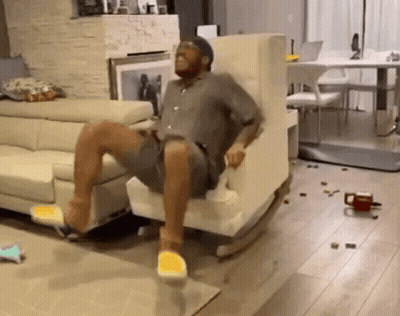 A Man Is Sitting In A Rocking Chair In A Living Room With A Couch . GIF