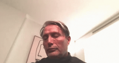 A Man Is Sitting In A Room With His Eyes Closed In Front Of A Painting Of A Face . GIF