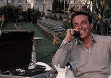 A Man Is Sitting In Front Of A Briefcase And Talking On A Phone GIF