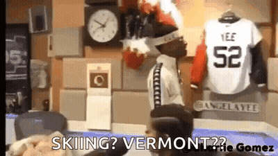 A Man Is Sitting In Front Of A Clock And A Jersey That Says ' Skiing ? Vermont ? ' GIF