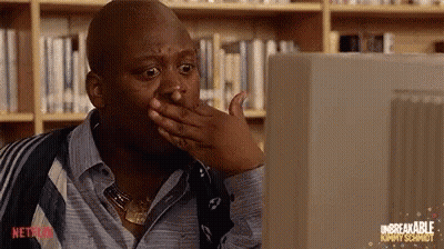 A Man Is Sitting In Front Of A Computer Screen And Covering His Mouth With His Hand . GIF