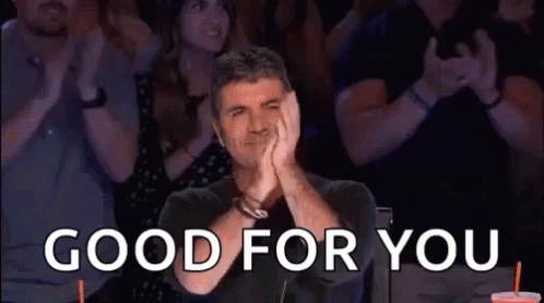 A Man Is Sitting In Front Of A Crowd Of People Applauding And Saying Good For You . GIF