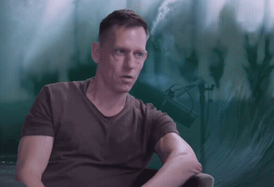 A Man Is Sitting In Front Of A Green Background GIF