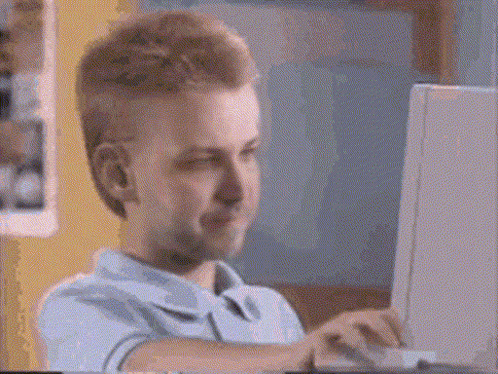 A Man Is Sitting In Front Of A Laptop Computer And Smiling . GIF