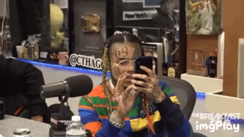 A Man Is Sitting In Front Of A Microphone Looking At His Phone GIF