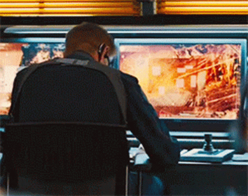 A Man Is Sitting In Front Of A Monitor With A Picture Of A Fire On It GIF