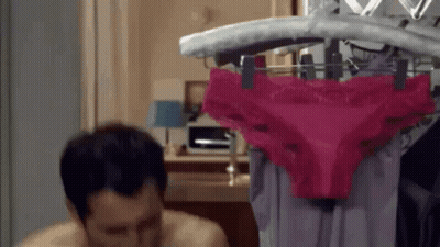 A Man Is Sitting In Front Of A Rack Of Pink Underwear . GIF