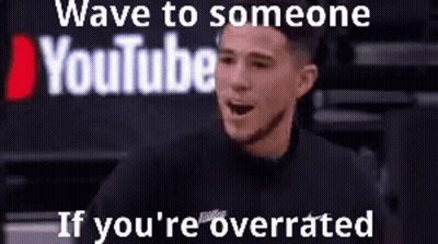 A Man Is Sitting In Front Of A Sign That Says Wave To Someone Youtube If You 'Re Overrated . GIF
