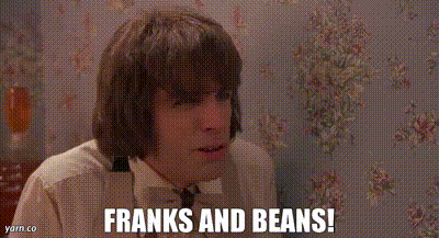 A Man Is Sitting In Front Of A Wall With Flowers On It And Says `` Franks And Beans '' . GIF
