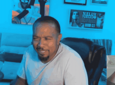 A Man Is Sitting In Front Of A Wall With Nelly Furtado Posters On It GIF