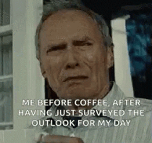 A Man Is Sitting In Front Of A Window Holding A Cup Of Coffee And Looking At The Camera . GIF