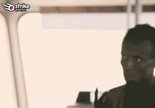 A Man Is Sitting In Front Of A Window With The Word Strike On The Bottom Right . GIF
