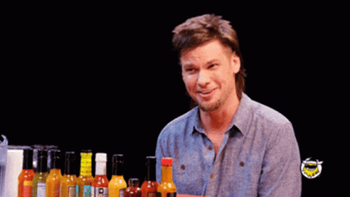 A Man Is Sitting In Front Of Bottles Of Hot Sauce And Says No Thanks GIF