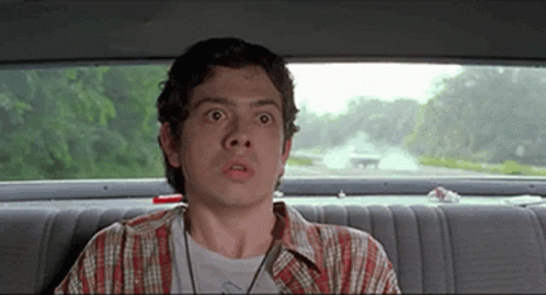 A Man Is Sitting In The Back Seat Of A Car And Looking Out The Window . GIF