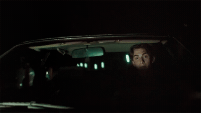A Man Is Sitting In The Back Seat Of A Car At Night Looking Out The Window . GIF